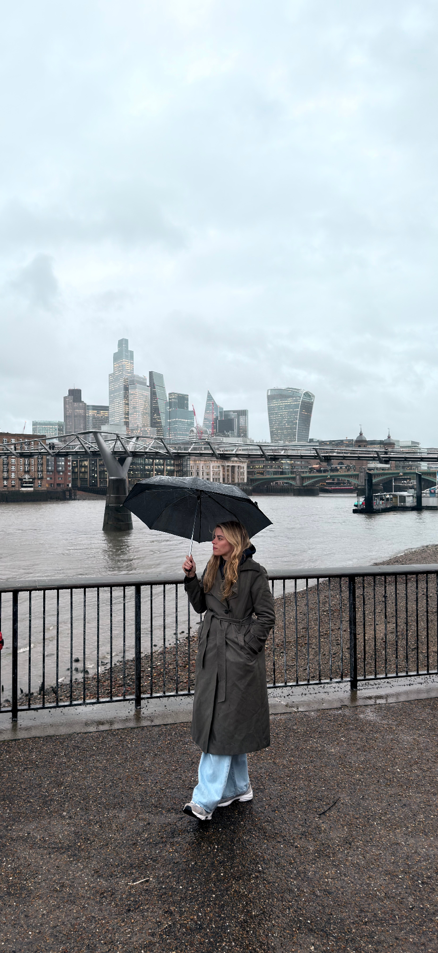 Walking along the Thames on a grey London afternoon, City skyline and Millennium Bridge in the distance.